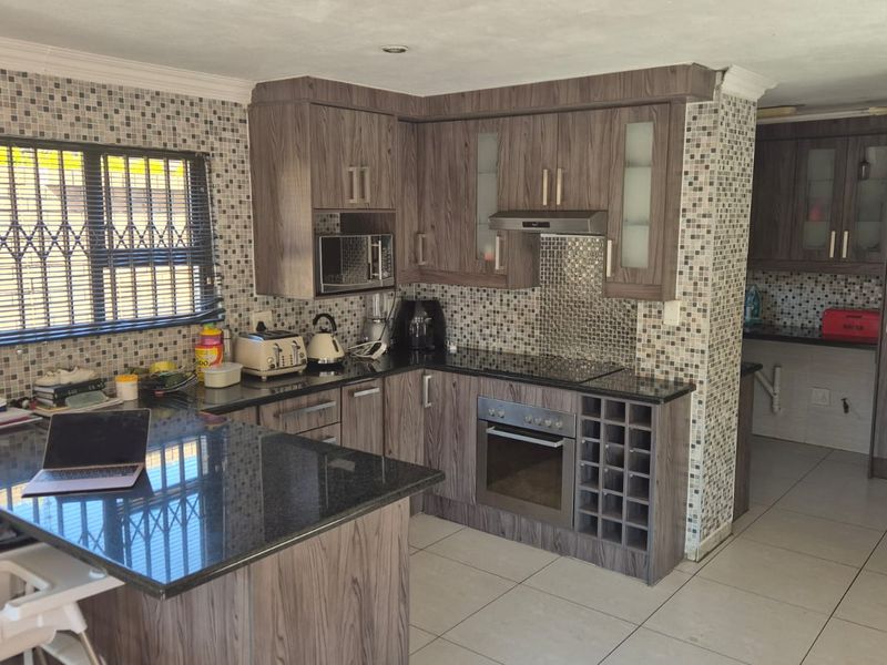 Modern kitchen featuring wood-grain cabinetry, granite countertops, mosaic tile backsplash, and integrated appliances, with an adjoining scullery area.