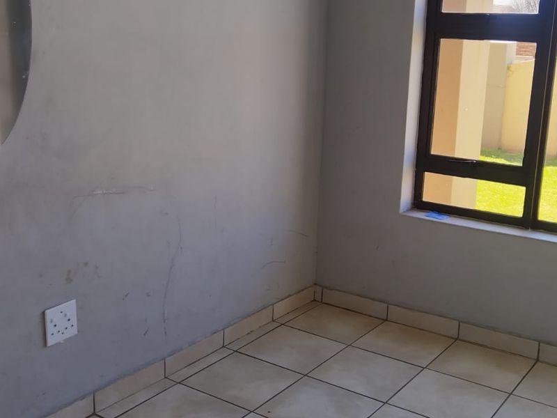 An empty bedroom featuring tiled flooring and an aluminium window frame, showing signs of wear on the wall surfaces.