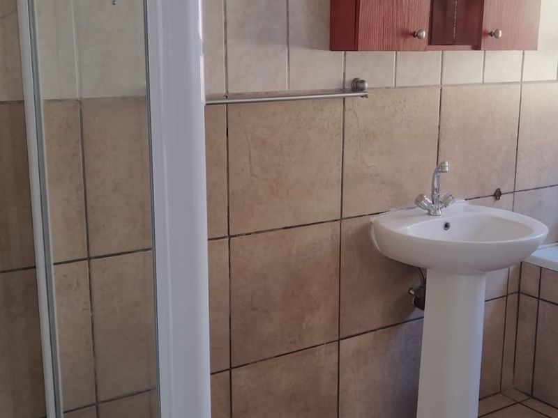 A functional bathroom featuring a pedestal basin, separate shower enclosure, and bathtub with neutral wall tiling and built-in cabinetry.