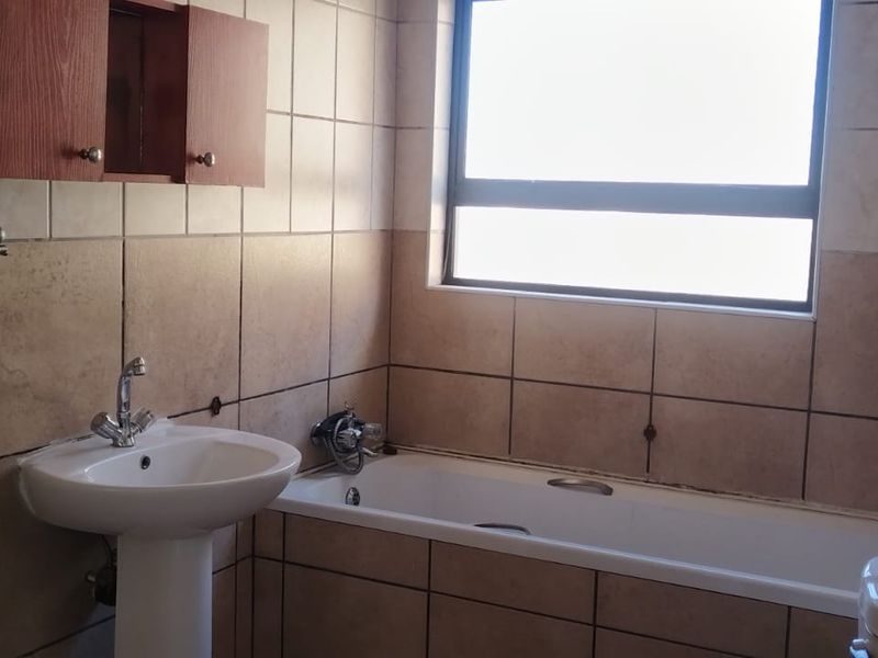 A functional bathroom featuring a pedestal basin, bathtub, and wall-mounted cabinetry with neutral wall tiling and natural light from a window.