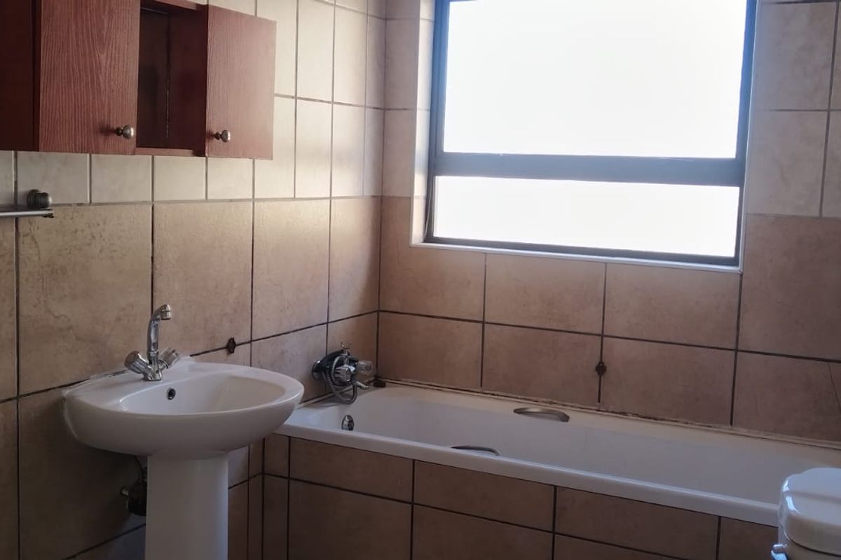 A functional bathroom featuring a pedestal basin, bathtub, and wall-mounted cabinetry with neutral wall tiling and natural light from a window.