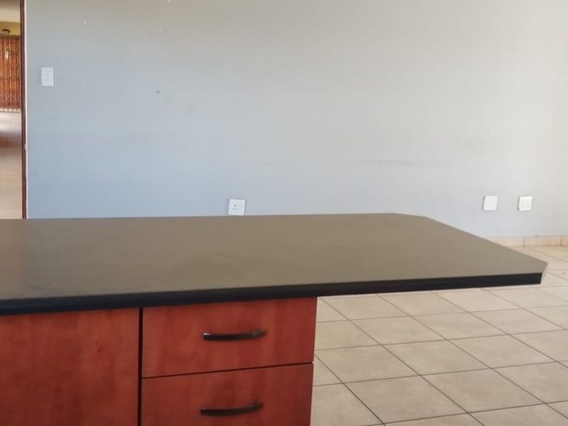 An open-plan living area featuring a kitchen island with dark laminate countertops and tiled flooring, offering a blank canvas for interior design.