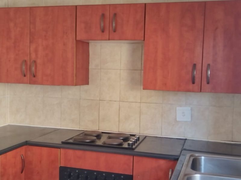 A functional kitchen featuring wood-look cabinetry, dark countertops, a built-in electric hob and oven, and a double stainless steel sink with tiled splashbacks.
