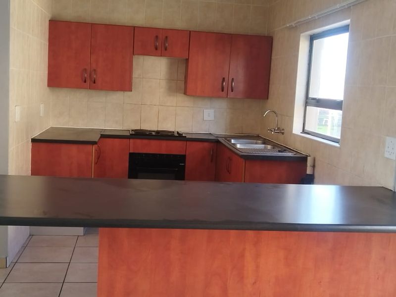 A functional kitchen featuring wood-finish cabinetry, dark laminate countertops, a breakfast bar, and built-in cooking appliances with tiled splashbacks.