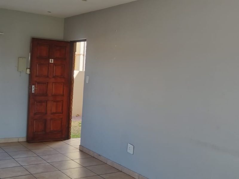 An empty living area featuring neutral wall paint, tiled flooring, and a timber entrance door with natural light from the window.