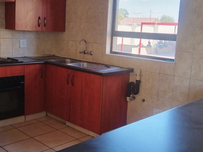 A functional kitchen featuring wooden cabinetry, dark laminate countertops, a built-in oven and hob, and tiled finishes throughout.