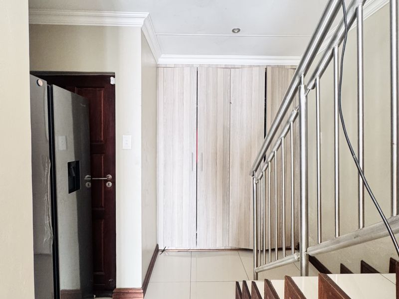 A hallway area featuring tiled flooring, built-in storage cupboards, and a stainless steel staircase railing, showing signs of minor ceiling damage.