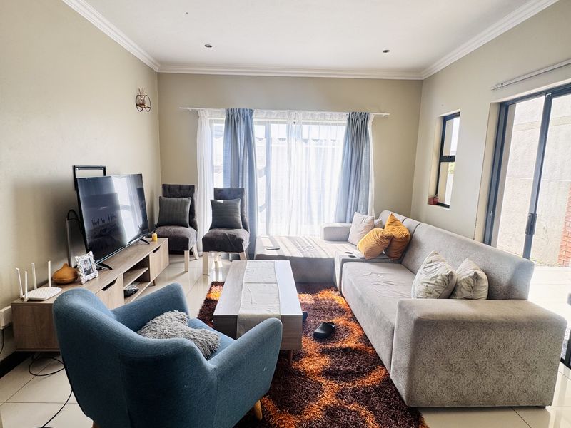 A bright and spacious living room featuring large format floor tiles, recessed downlighting, and a sliding glass door providing access to the outdoor area.