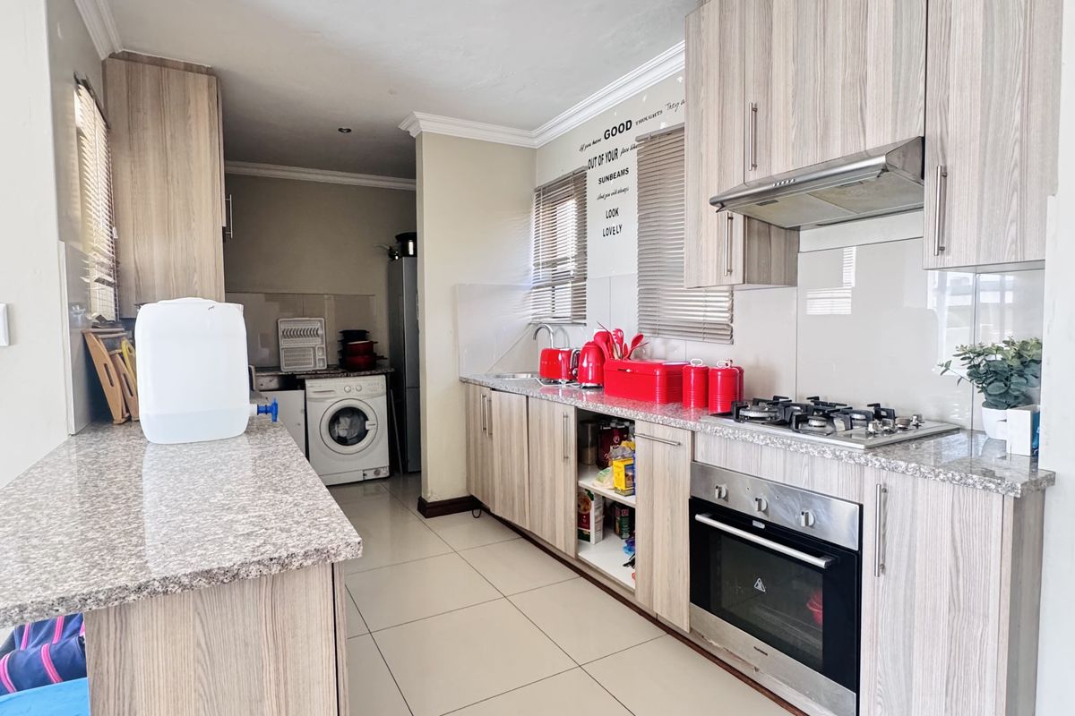 Modern kitchen featuring light wood-grain cabinetry, granite countertops, integrated gas hob, electric oven, and a dedicated laundry area with tiled flooring throughout.