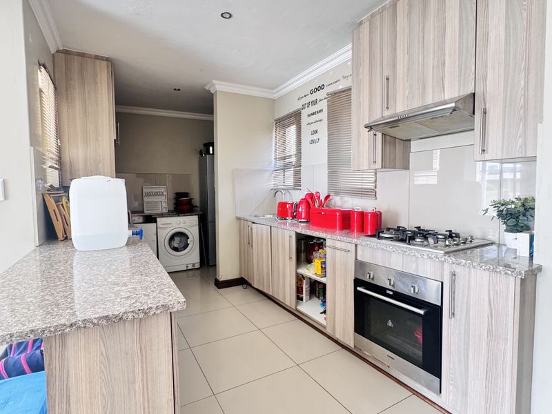 Modern kitchen featuring light wood-grain cabinetry, granite countertops, integrated gas hob, electric oven, and a dedicated laundry area with tiled flooring throughout.