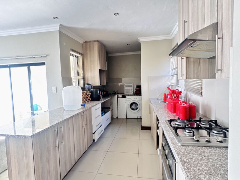 Modern kitchen featuring granite countertops, light wood-finish cabinetry, gas hob, extractor fan, and integrated laundry area with tiled flooring throughout.