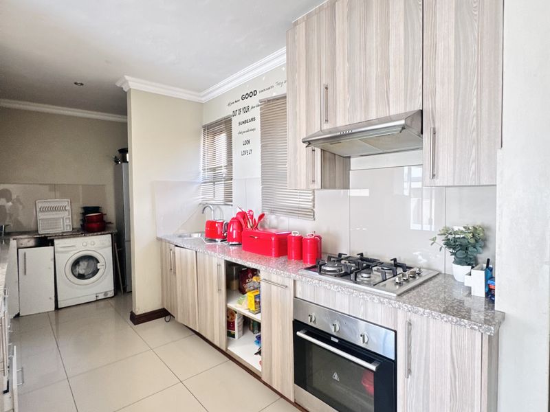 A functional kitchen featuring wood-look cabinetry, granite countertops, a gas hob, built-in oven, and an integrated laundry area with tiled flooring throughout.