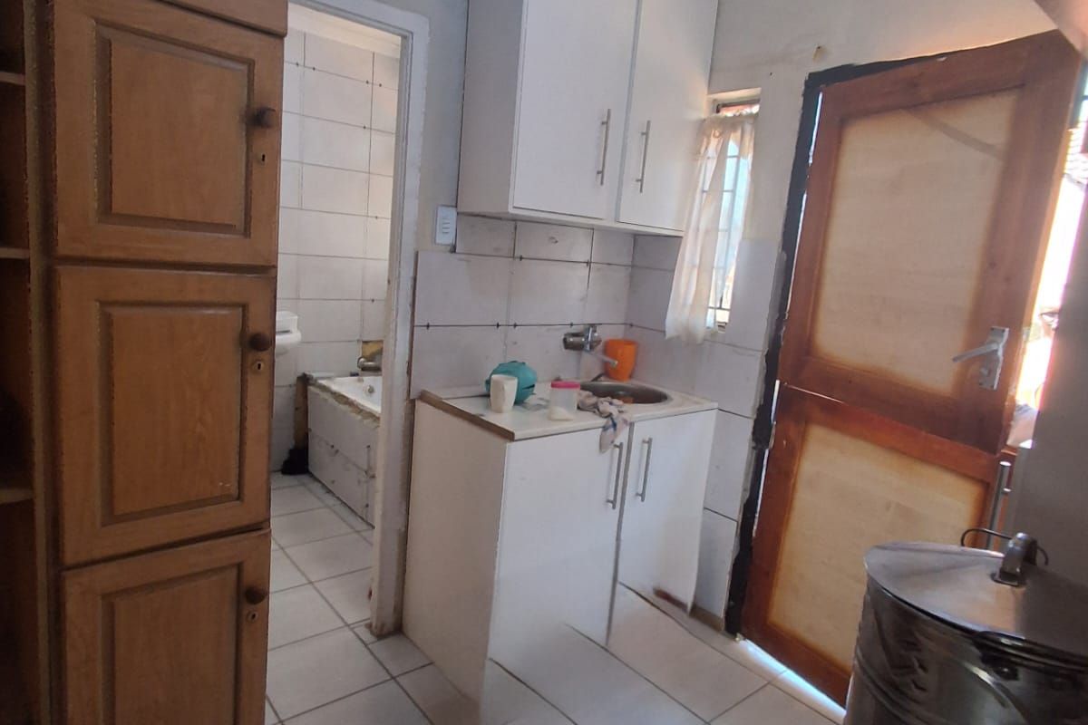 A compact kitchen area featuring tiled floors, built-in cabinetry, and a sink, with direct access to an adjacent bathroom.