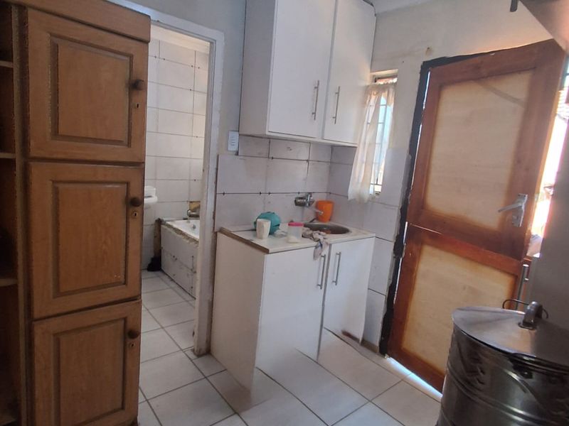 A compact kitchen area featuring tiled floors, built-in cabinetry, and a sink, with direct access to an adjacent bathroom.