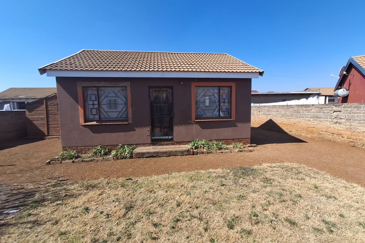 Rear view of a detached house featuring a tiled roof, security bars on windows, and a surrounding brick boundary wall.