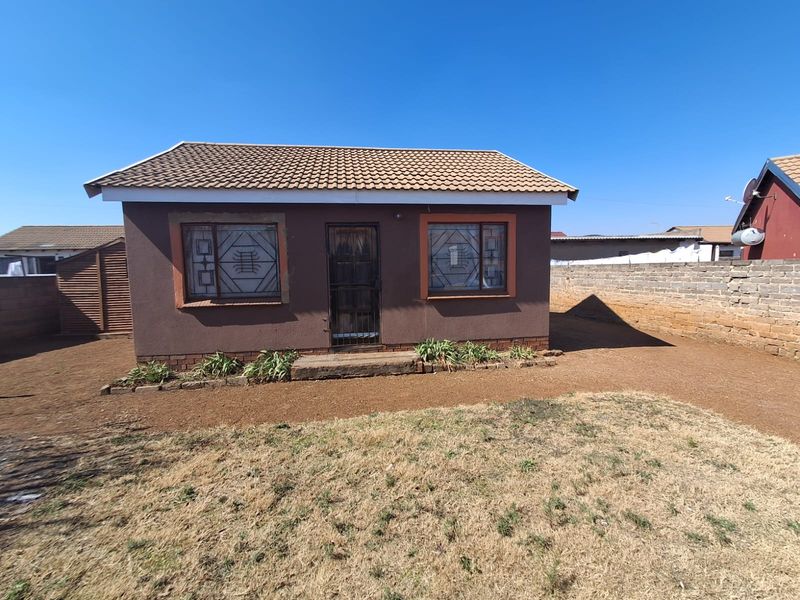 Rear view of a detached house featuring a tiled roof, security bars on windows, and a surrounding brick boundary wall.
