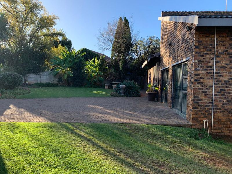 A well-maintained rear exterior featuring a brick facade, paved patio area, and established garden with sliding glass doors providing access to the home.