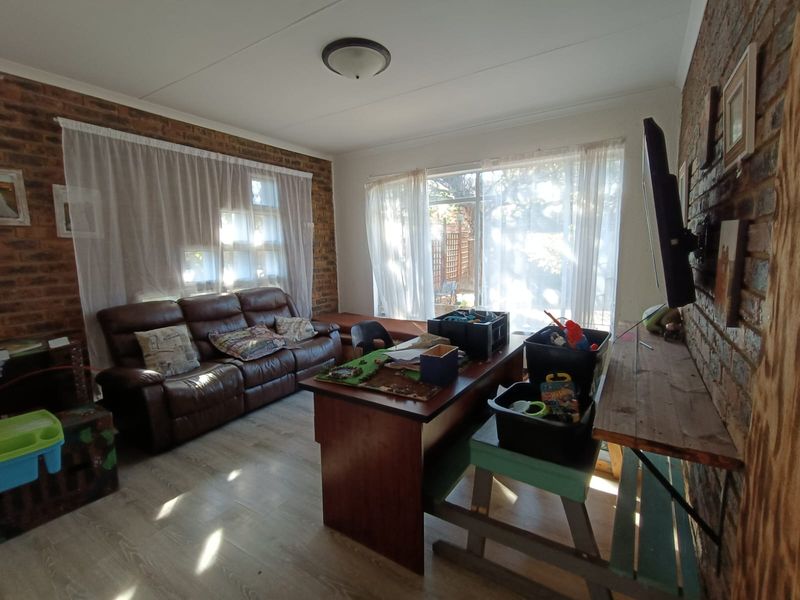A living room featuring exposed brick walls, laminate flooring, and large windows that provide ample natural light.