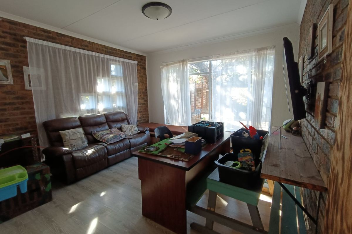 A living room featuring exposed brick walls, laminate flooring, and large windows that provide ample natural light.