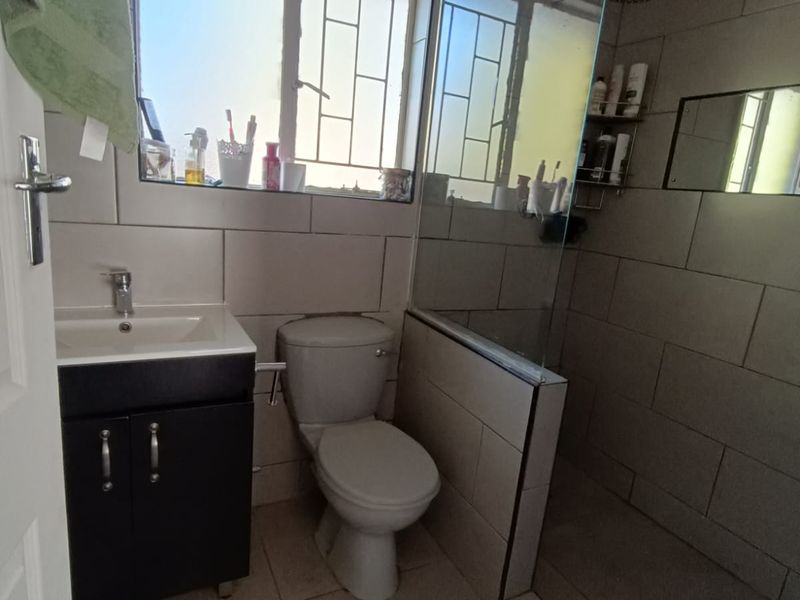 A functional bathroom featuring a vanity cabinet, toilet, and a walk-in shower with a glass screen, finished with neutral wall and floor tiles.