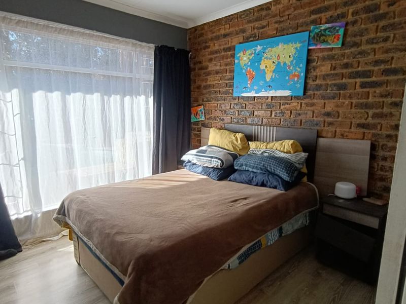 A bedroom featuring an exposed brick feature wall, light-toned laminate flooring, and a large window allowing for natural light.