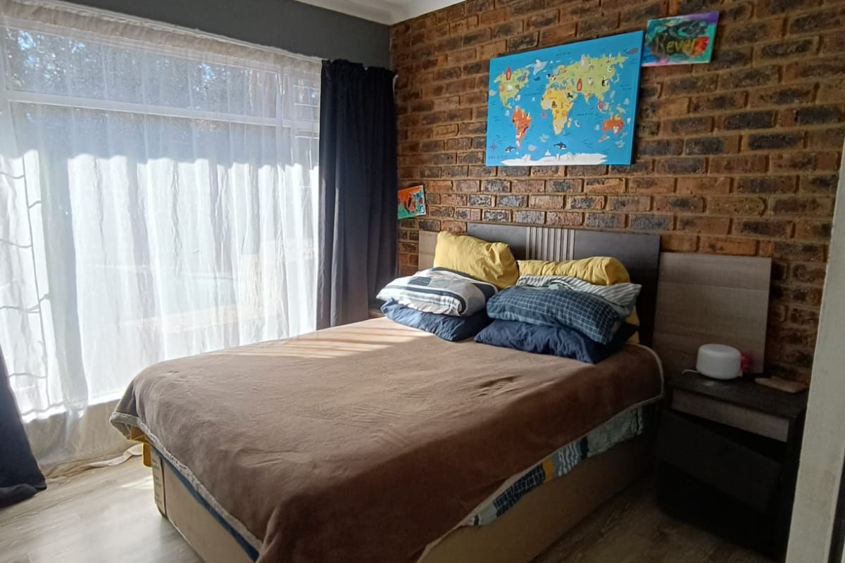 A bedroom featuring an exposed brick feature wall, light-toned laminate flooring, and a large window allowing for natural light.