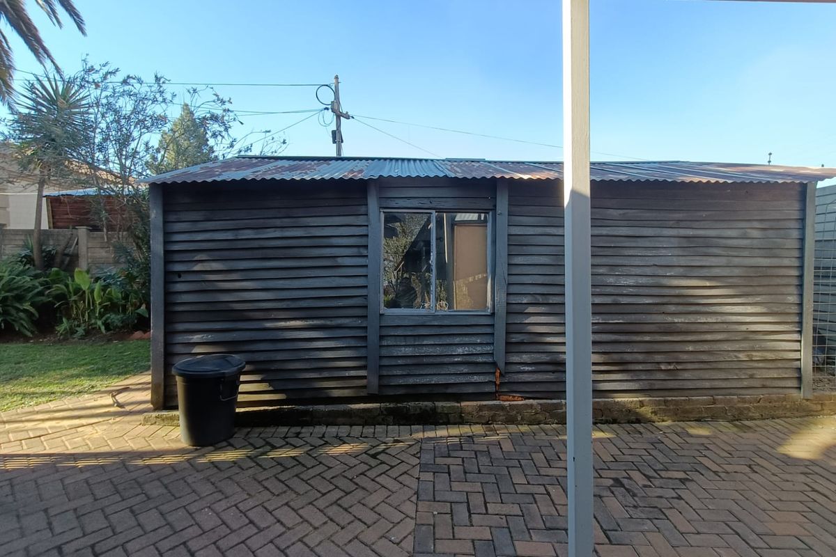 Rear view of a timber-clad outbuilding featuring a corrugated iron roof and paved patio area, showing signs of significant weathering and wear.