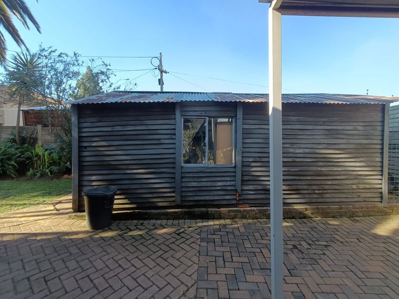 Rear view of a timber-clad outbuilding featuring a corrugated iron roof and paved patio area, showing signs of significant weathering and wear.