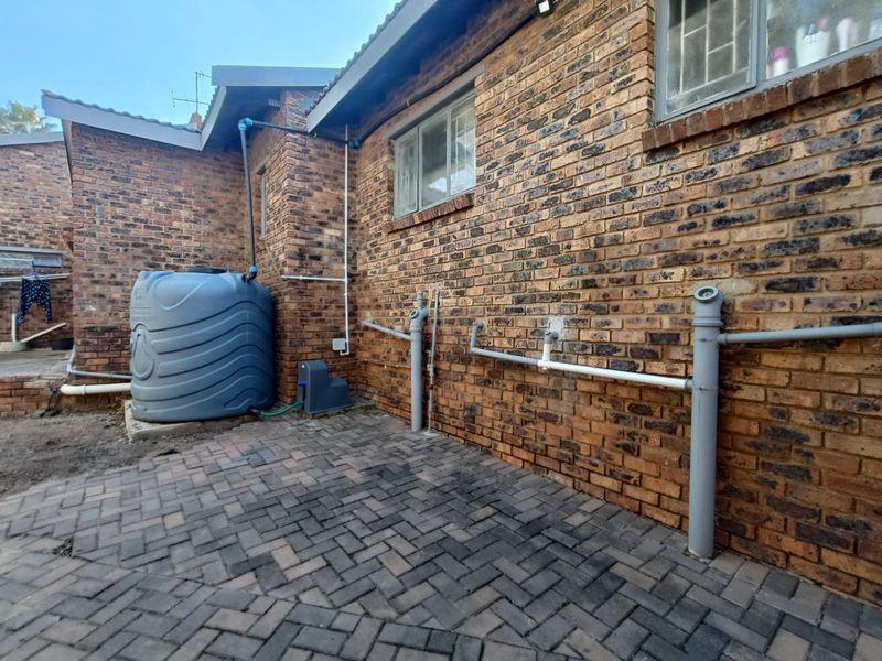 Rear exterior area featuring a brick facade, paved courtyard, and a large water storage tank with external plumbing infrastructure.