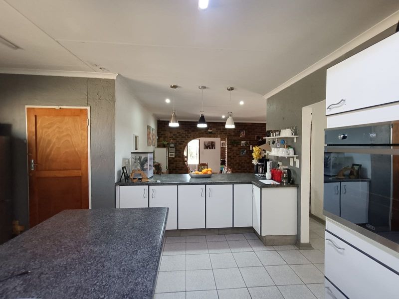 A functional kitchen featuring built-in cabinetry, a central island, tiled flooring, and a distinctive exposed brick feature wall with pendant lighting.