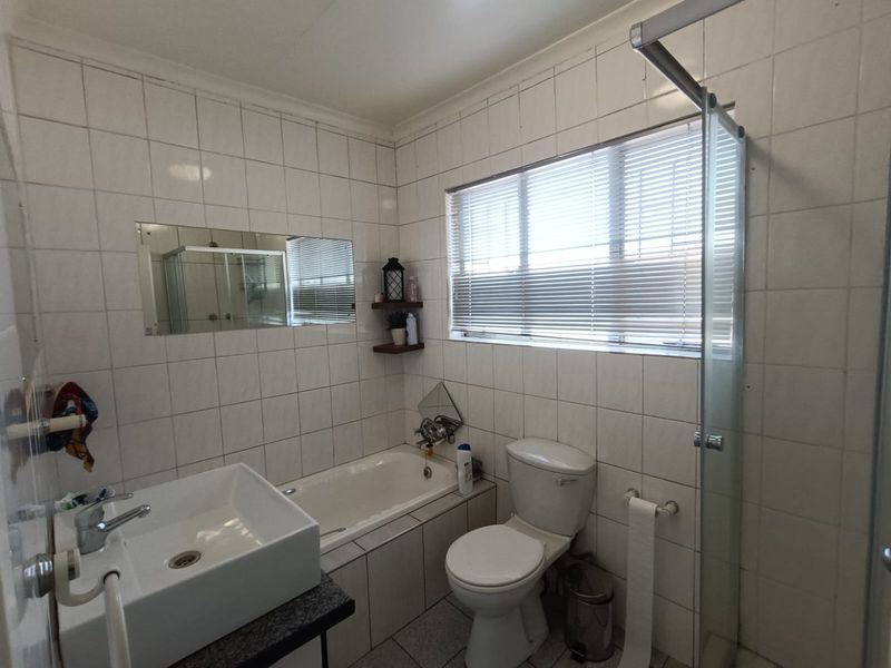 A functional bathroom featuring a built-in bathtub, separate glass shower enclosure, wall-mounted basin, and tiled finishes throughout.