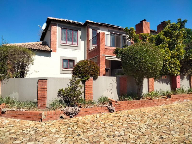 Front elevation of a townhouse featuring a brick and plaster facade, a balcony, and a paved driveway with a surrounding boundary wall.