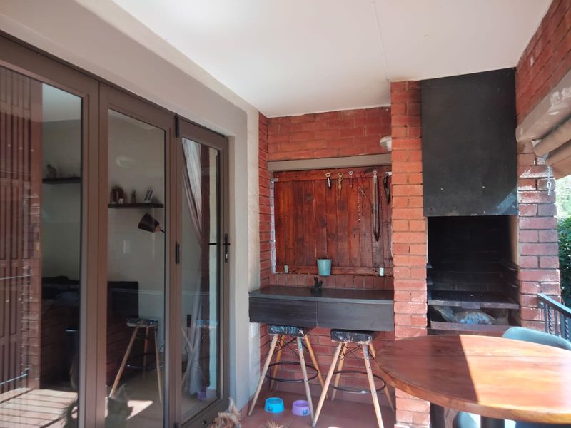 Covered patio area featuring a built-in brick braai, tiled flooring, and large sliding glass doors providing seamless access to the interior living space.