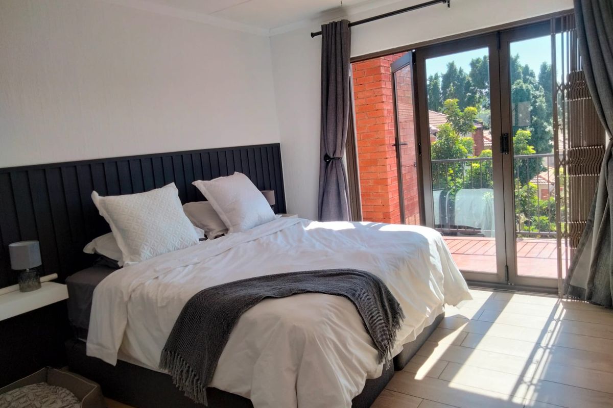 A well-lit bedroom featuring tiled flooring, a custom built-in headboard, and direct access to a private balcony through sliding glass doors.