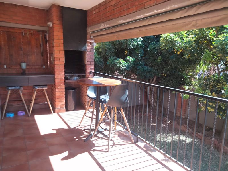 Covered patio area featuring a built-in brick braai, tiled flooring, and a metal balustrade overlooking the garden.