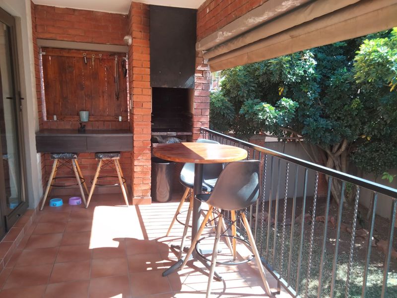 Covered patio featuring a built-in brick braai, tiled flooring, and a metal balustrade, overlooking a private garden area.