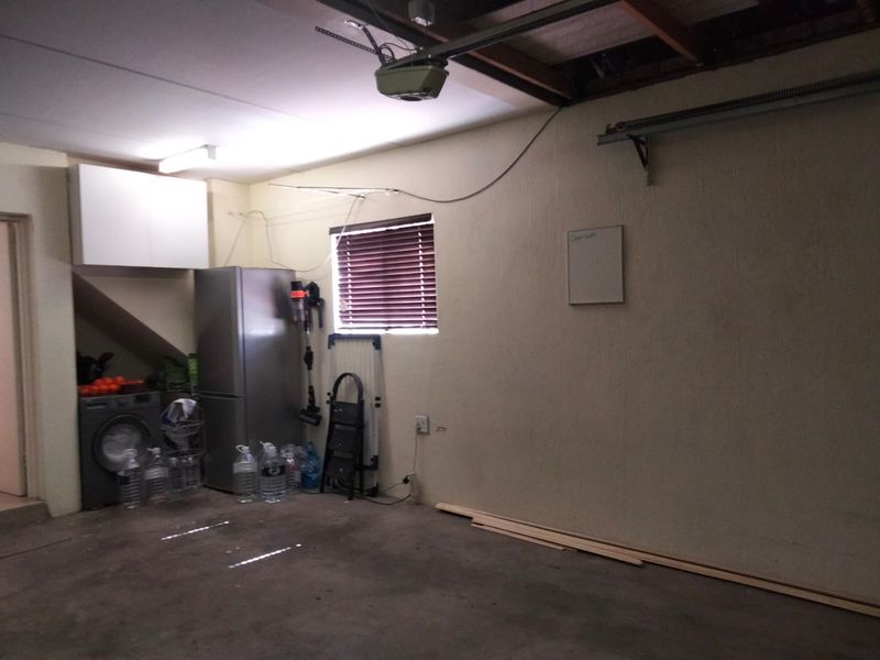 A functional garage space featuring exposed ceiling beams, built-in storage cabinetry, and a window with blinds, providing practical utility and storage potential.