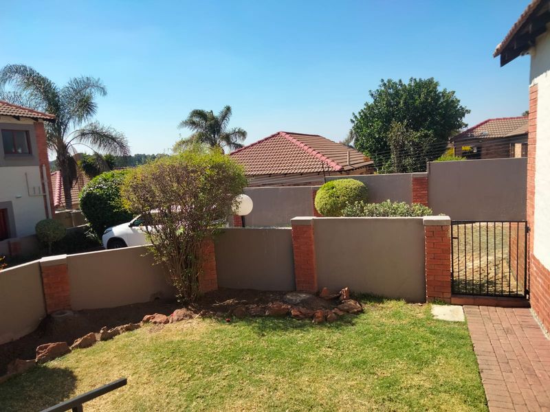 A private rear garden area featuring a well-maintained lawn, brick boundary walls with integrated pillars, and a secure metal pedestrian gate.