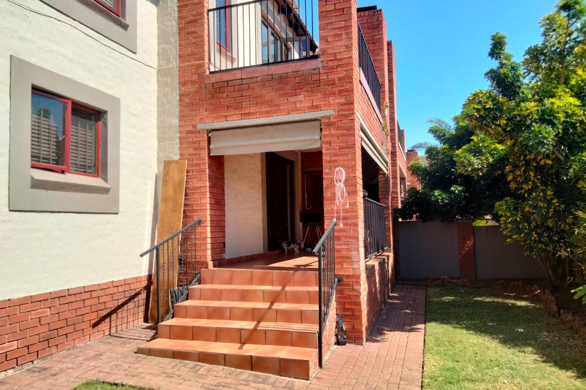 Rear exterior view of a townhouse featuring a brick facade, tiled staircase leading to a patio, metal railings, and a small private garden area.