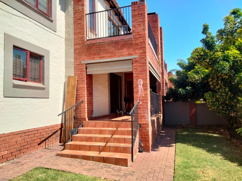 Rear exterior view of a townhouse featuring a brick facade, tiled staircase leading to a patio, metal railings, and a small private garden area.