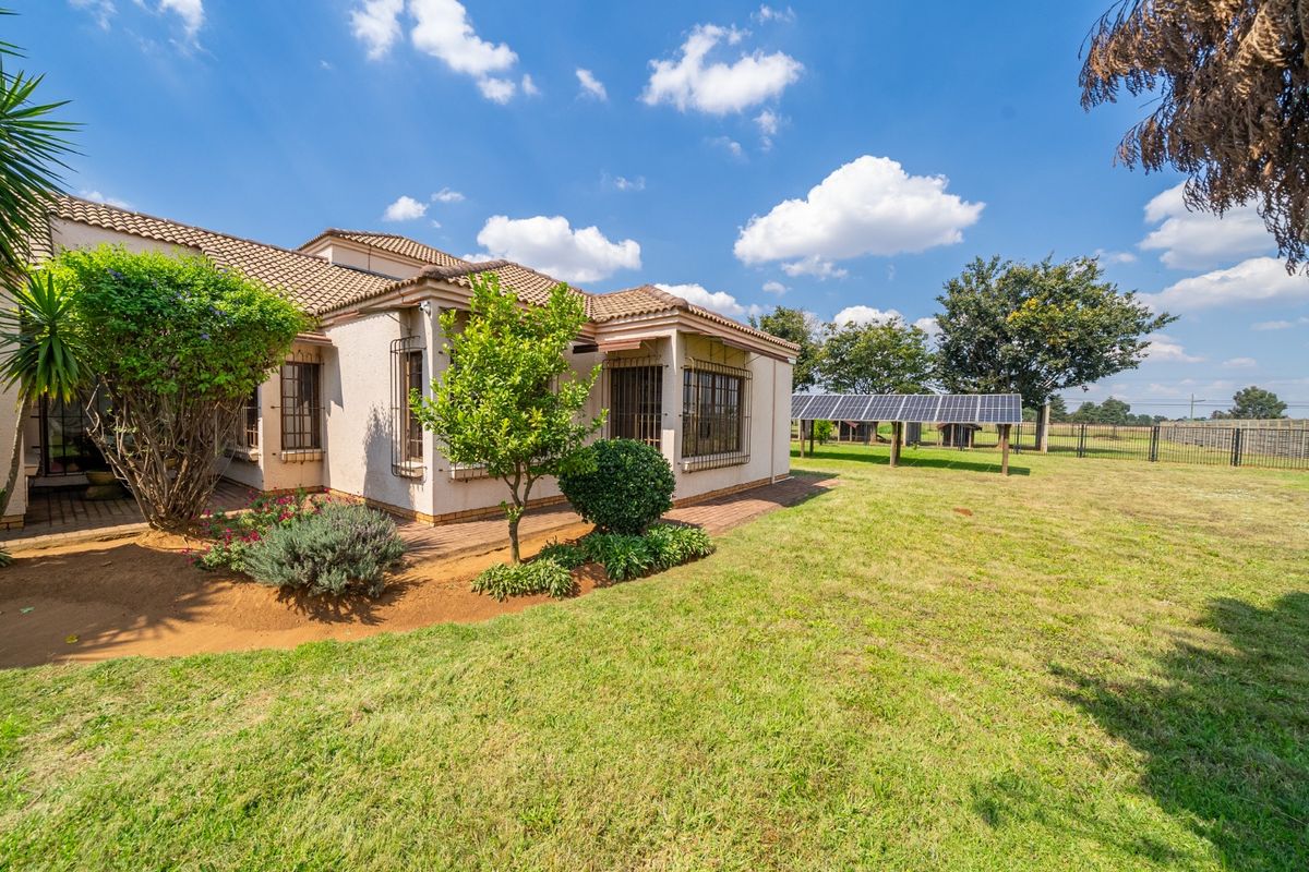 Rear view of the property featuring a tiled roof, security bars on windows, a paved patio area, and a ground-mounted solar panel array.