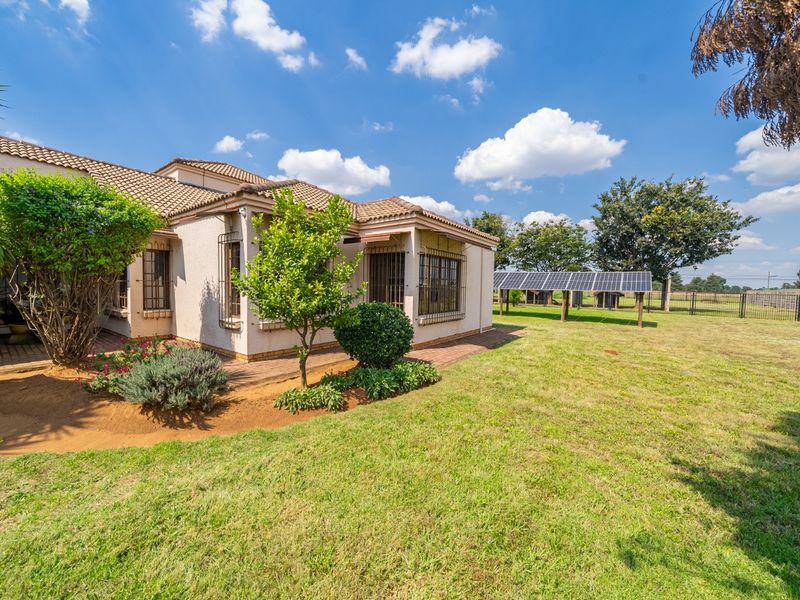 Rear view of the property featuring a tiled roof, security bars on windows, a paved patio area, and a ground-mounted solar panel array.