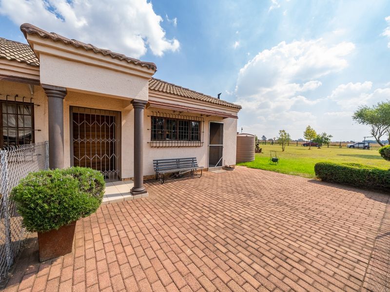 A covered patio area with brick paving, featuring security gates and bars, overlooking a spacious garden with a water tank.