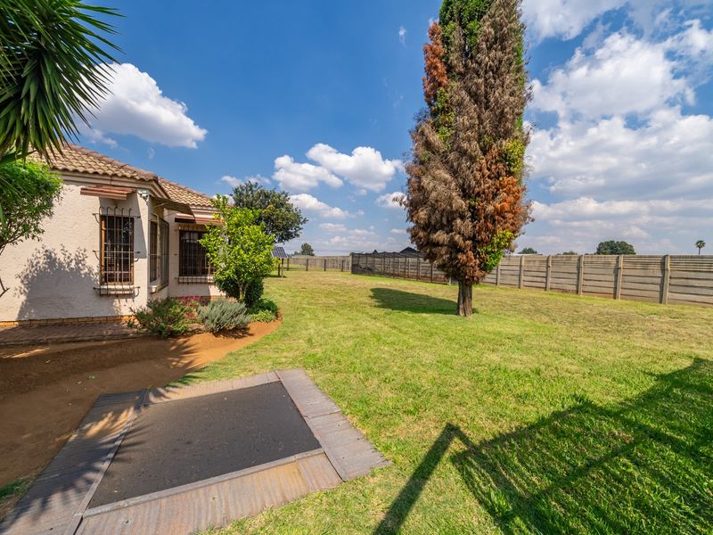 A spacious rear garden area featuring a lawn, precast concrete boundary wall, and a view of the side elevation of the house with security bars.