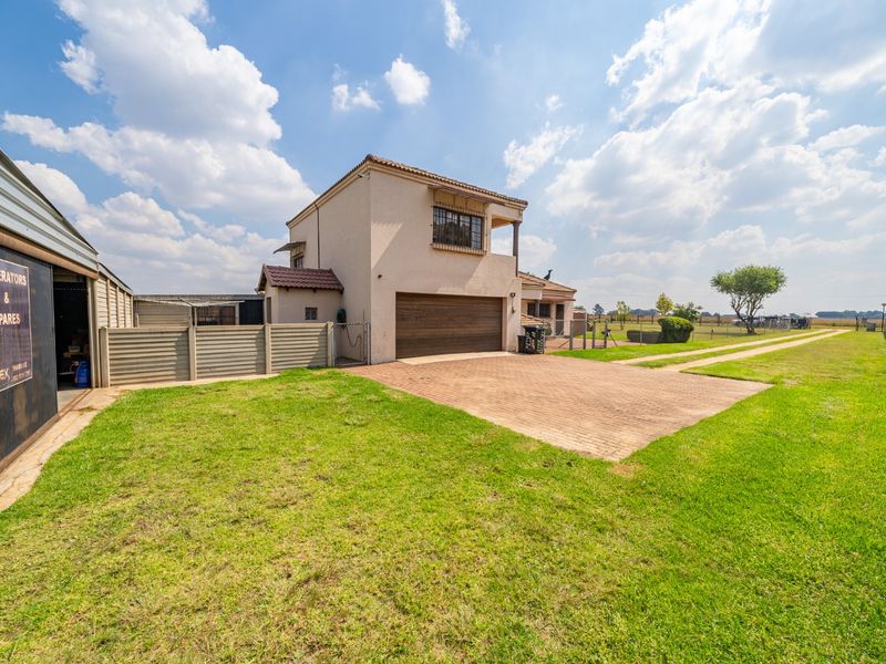 Front exterior view of a small holding property featuring a double garage, paved driveway, and adjacent metal storage shed with perimeter electric fencing.