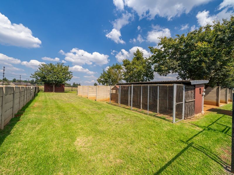 Spacious rear garden area featuring a well-maintained lawn, precast concrete boundary walls, and a series of metal mesh kennel enclosures.