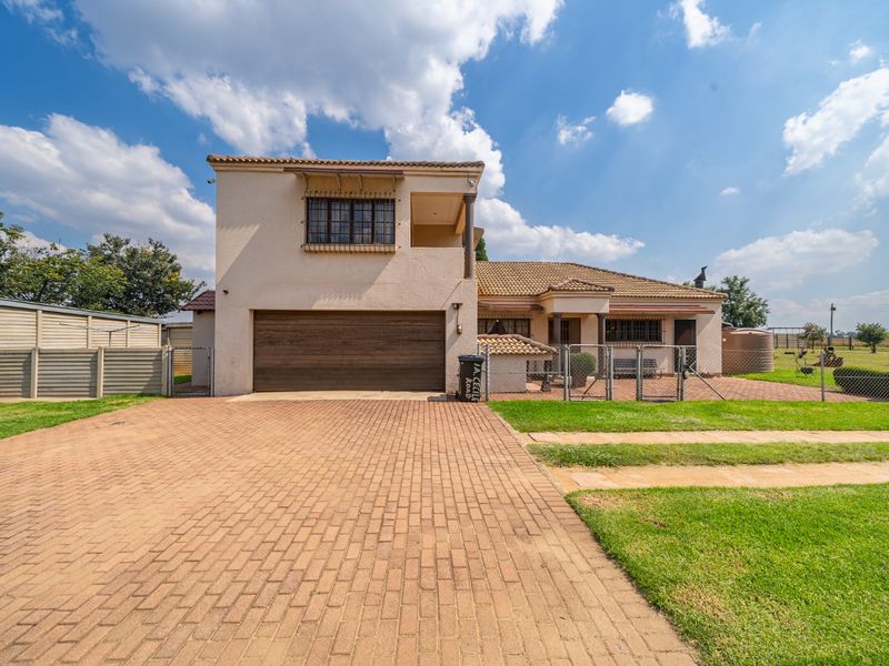 Front view of a double-story small holding property featuring a paved driveway, double garage, tiled roof, and secure perimeter fencing.