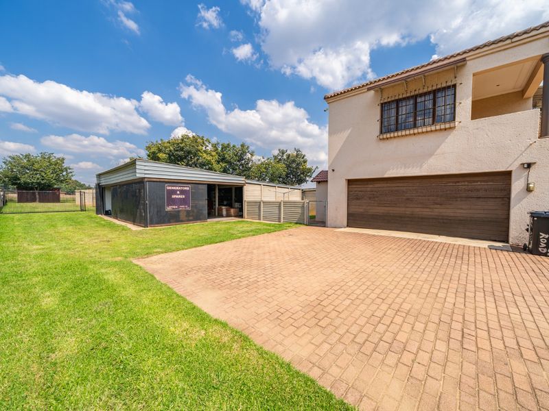 Front exterior view of the property featuring a paved driveway, double garage, and a separate outbuilding on a spacious lawn.