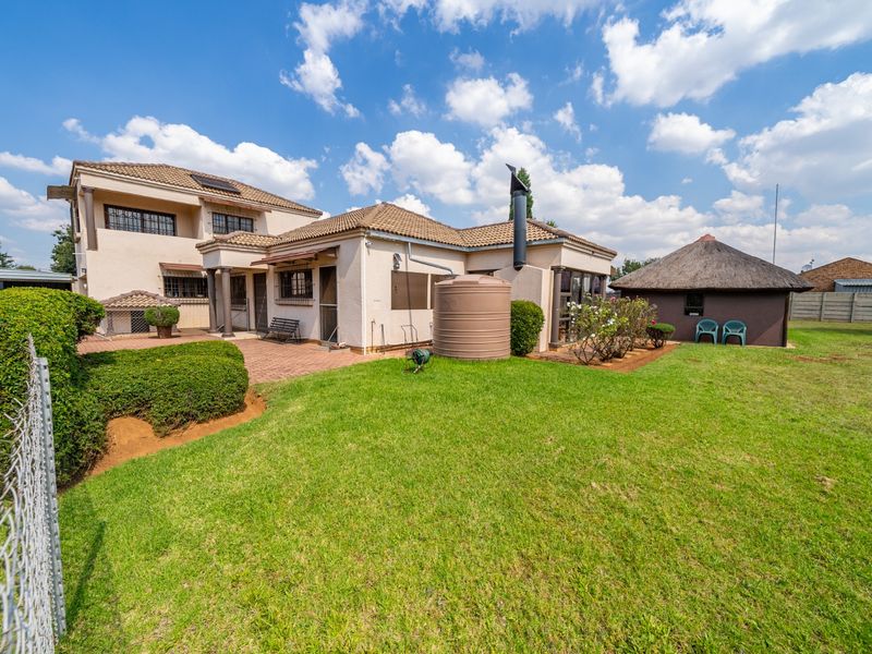 Rear view of the property featuring a paved patio, a large lawn, a water storage tank, and a separate thatched lapa structure.
