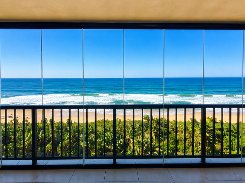 A spacious balcony featuring a glass-enclosed system and metal balustrade, offering panoramic, unobstructed views of the ocean and coastline.